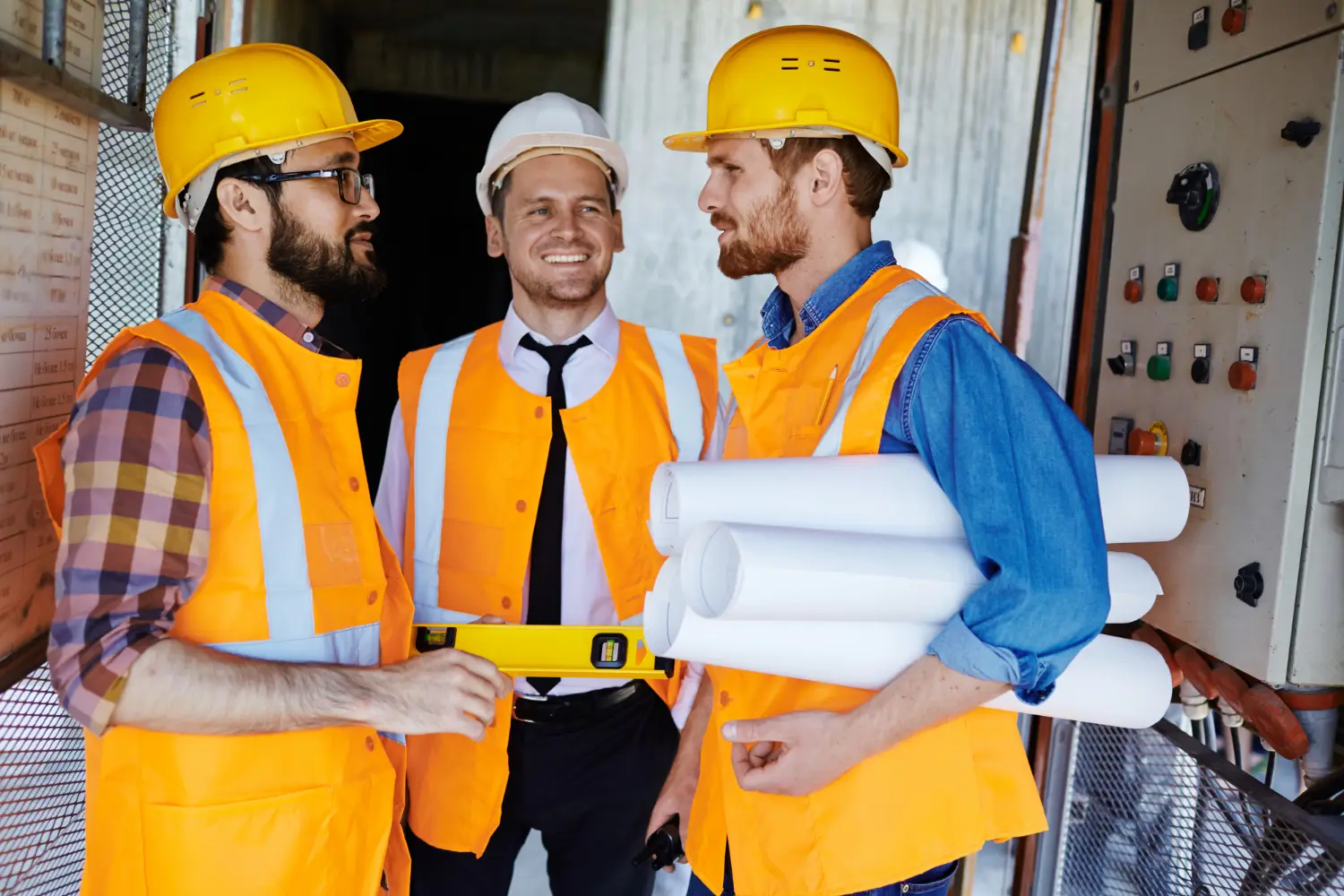 A diverse team of construction workers wearing hard hats and safety vests huddling together for a safety meeting.
